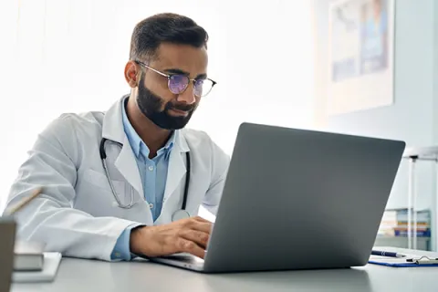 Medical professional in a white coat looking at an open laptop